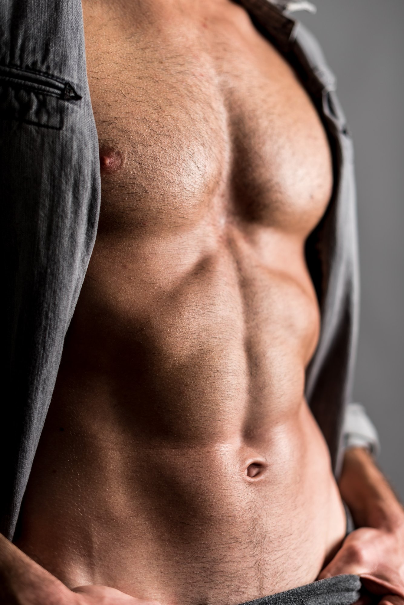 Muscular young man in grey shirt with trimmed short (Stubble Look) chest hair.