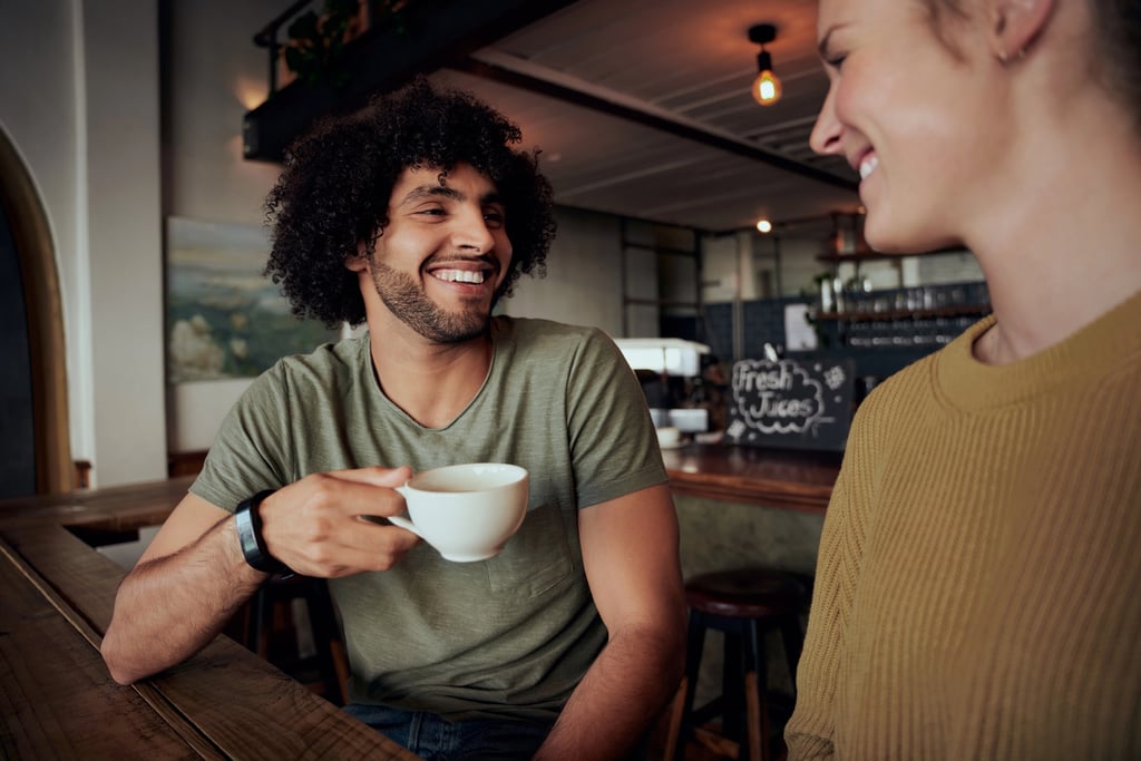 Handsome young man dating in his 20s holding coffee cup sitting with beautiful woman and talking in cafe