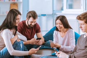A group of young adults sitting together casually, smiling while using smartphones during a relaxed therapy group session