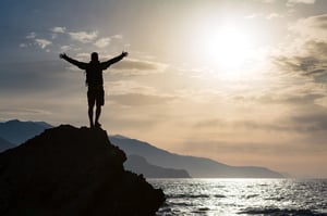 Man standing with arms outstretched on a mountaintop at sunrise, symbolizing freedom, achievement, and powerful inspirational quotes about life.