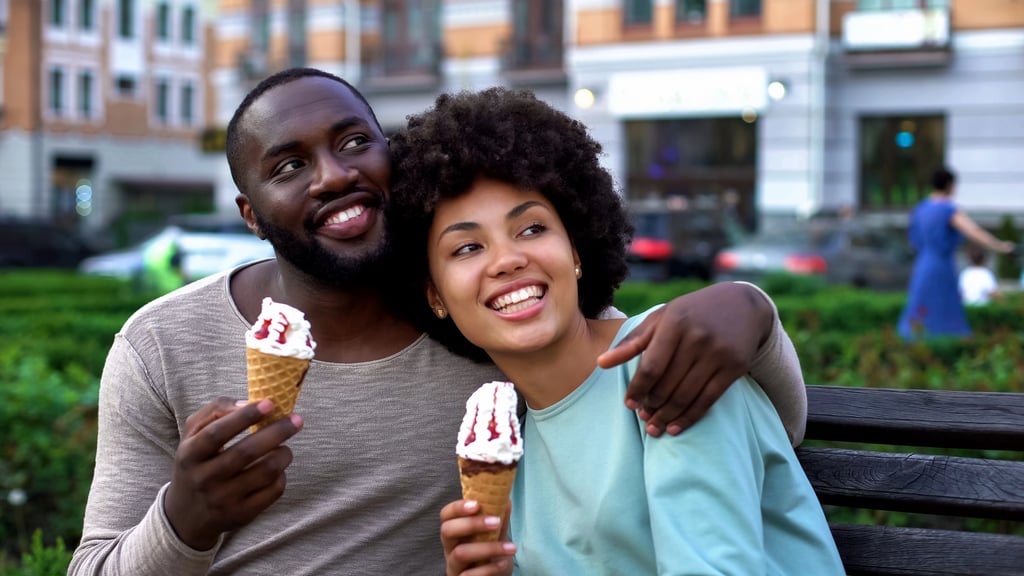 A happy couple laughing on bench enjoying romantic second date with ice-cream.