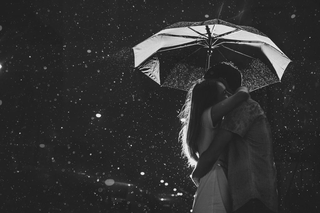 A girl is hugging her boyfriend in the rain while they stand under an umbrella.