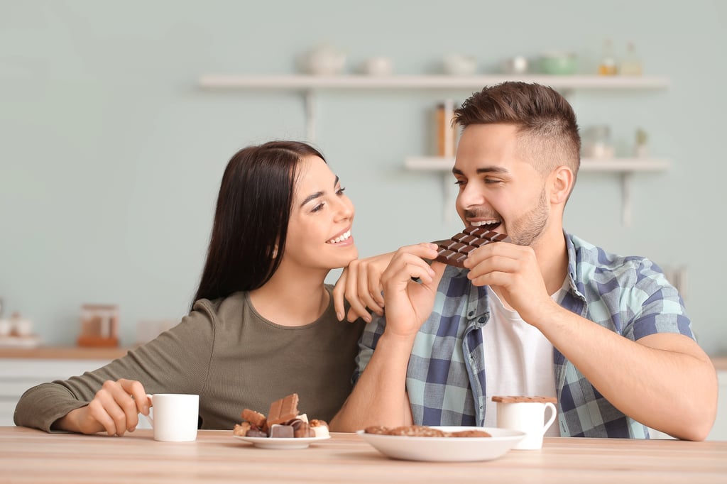 A beautiful young couple eating chocolate in kitchen.