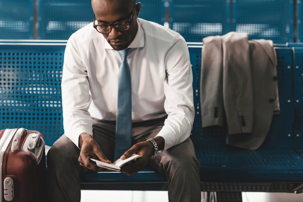 A businessman reading a book while waiting for flight at airport lobby.