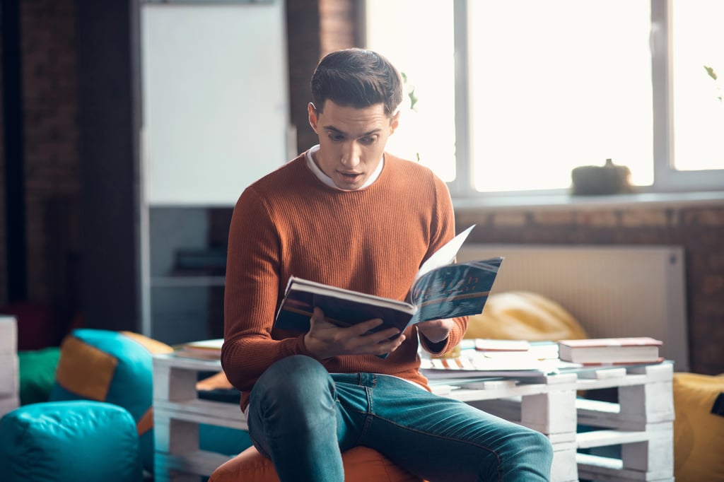 A young man feeling surprised while reading a book.