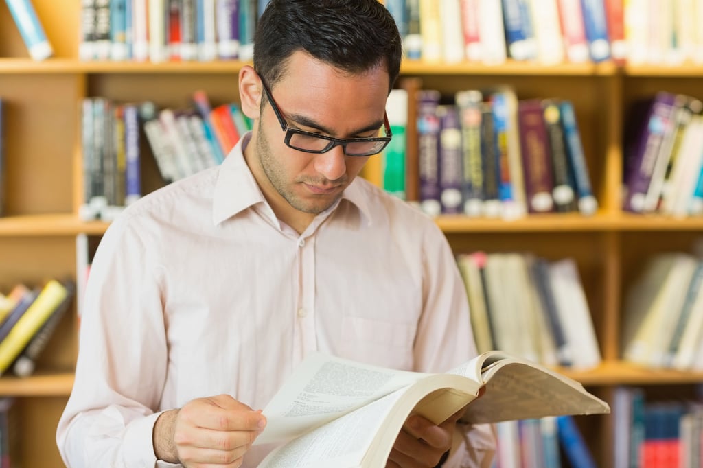 A concentrated man reading a book in library.