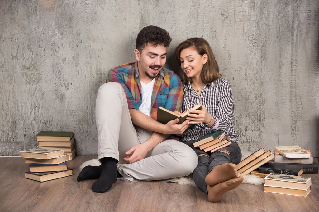 A young couple sitting on the floor and reading a book.