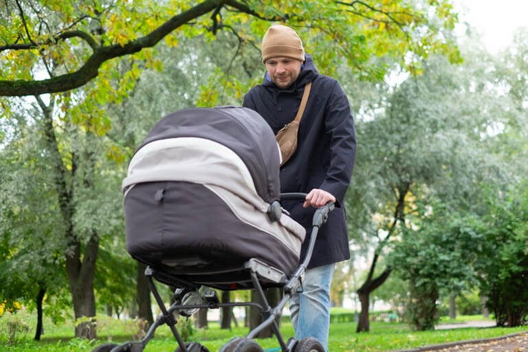 Man pushing a baby stroller in a green park, illustrating hands-on fatherhood often associated with Swedish men