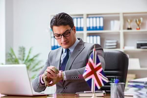 A suited professional at a desk with a UK flag, reviewing documents and checking his watch, symbolising UK civil partner visa requirements