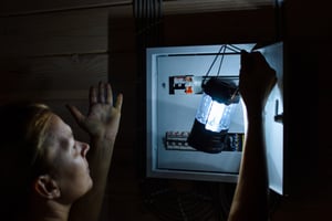 A man inspecting a home electrical panel with a flashlight during an electrical safety check