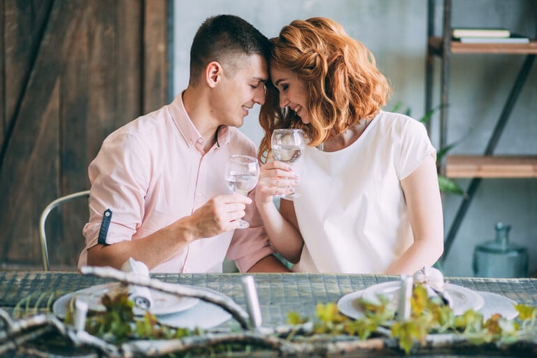 Affluent couple on a romantic date, leaning close and toasting with wine glasses in an intimate setting