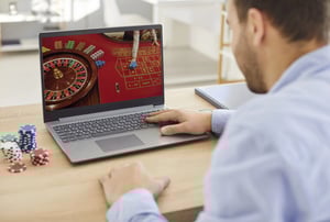Man using a laptop to play online roulette with casino chips nearby