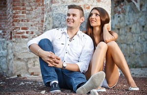 A smiling, idealized couple sitting against a brick wall, representing the type of polished imagery often used as synthetic content in online dating