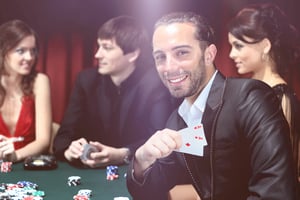 A smiling man in a suit holding a winning pair of aces at a casino table, illustrating the social and immersive experience of live dealer games