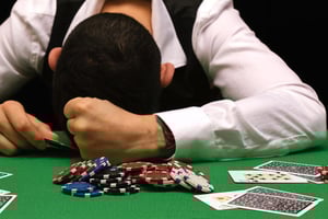 Casino chips and cards on the table with a stressed man, representing gambling risk, money loss, and emotional decision-making