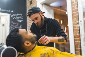Barber trimming a client’s beard in a modern barbershop, highlighting how barbershops have become social hubs for men to relax, interact, and connect.