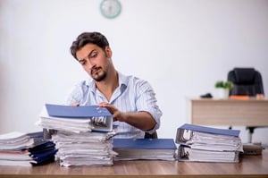 Overwhelmed businessman at a desk buried in paperwork, highlighting the need for better document workflow.