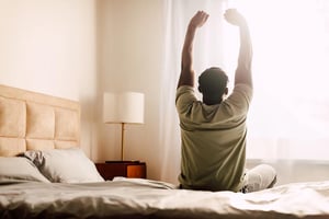 Man stretching in bed at sunrise, building a consistent morning routine with natural light, calm focus, and healthy daily habits
