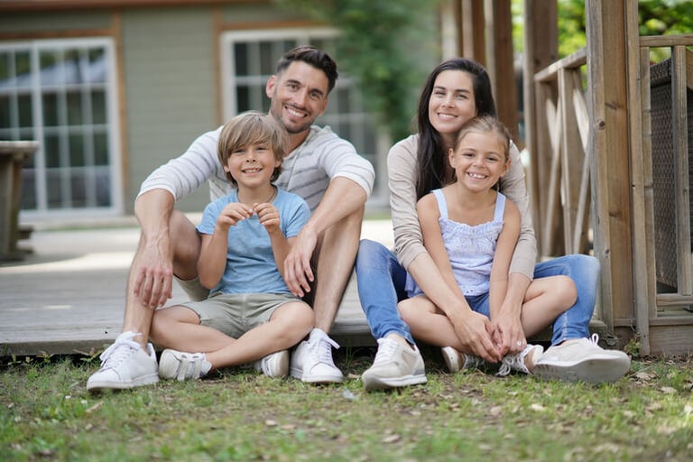 Happy family sitting together outside their home, representing support, stability, and a nurturing environment aligned with group home program values.