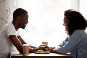 Couple sitting across from each other at a café table, discussing modern dating challenges and relationship expectations in a relaxed social setting.