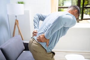 A man holding his lower back in pain while standing in a living room, illustrating common lower back pain issues and discomfort.