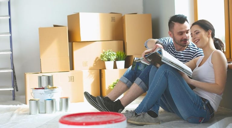 A couple sitting among moving boxes and paint cans while planning a home or business storage and renovation setup.