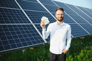 Man standing beside rooftop solar panels, representing the difference between premium high-performance solar technology and lower-cost solar panel options.