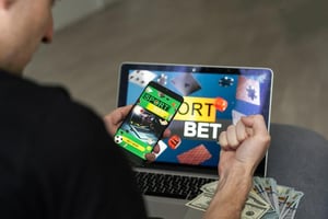 Man using a smartphone and a laptop to place sports bets online.