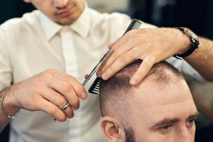 Close-up of a barber precisely cutting a balding man’s hair with shears and a comb, showing grooming for thinning hair.