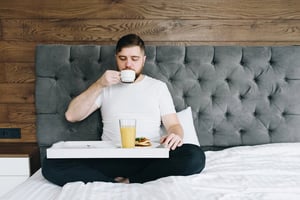 A man sitting in bed with a cup of coffee and a newspaper, representing unconventional morning habits for productivity and focus.