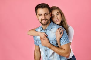 Young couple embracing and smiling against a pink background for Secretmeet review and online dating platform.