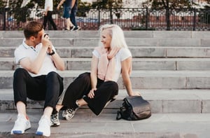 A young couple interacting on outdoor steps as the man takes a photo, illustrating a realistic connection and healthy standards.