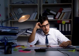 A stressed office worker sitting late at a cluttered desk, overwhelmed by client work and paperwork.